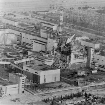 Celkový pohled na Černobylskou jadernou elektrárnu krátce po výbuchu jednoho z reaktorů (šipka označuje místo havárie)
