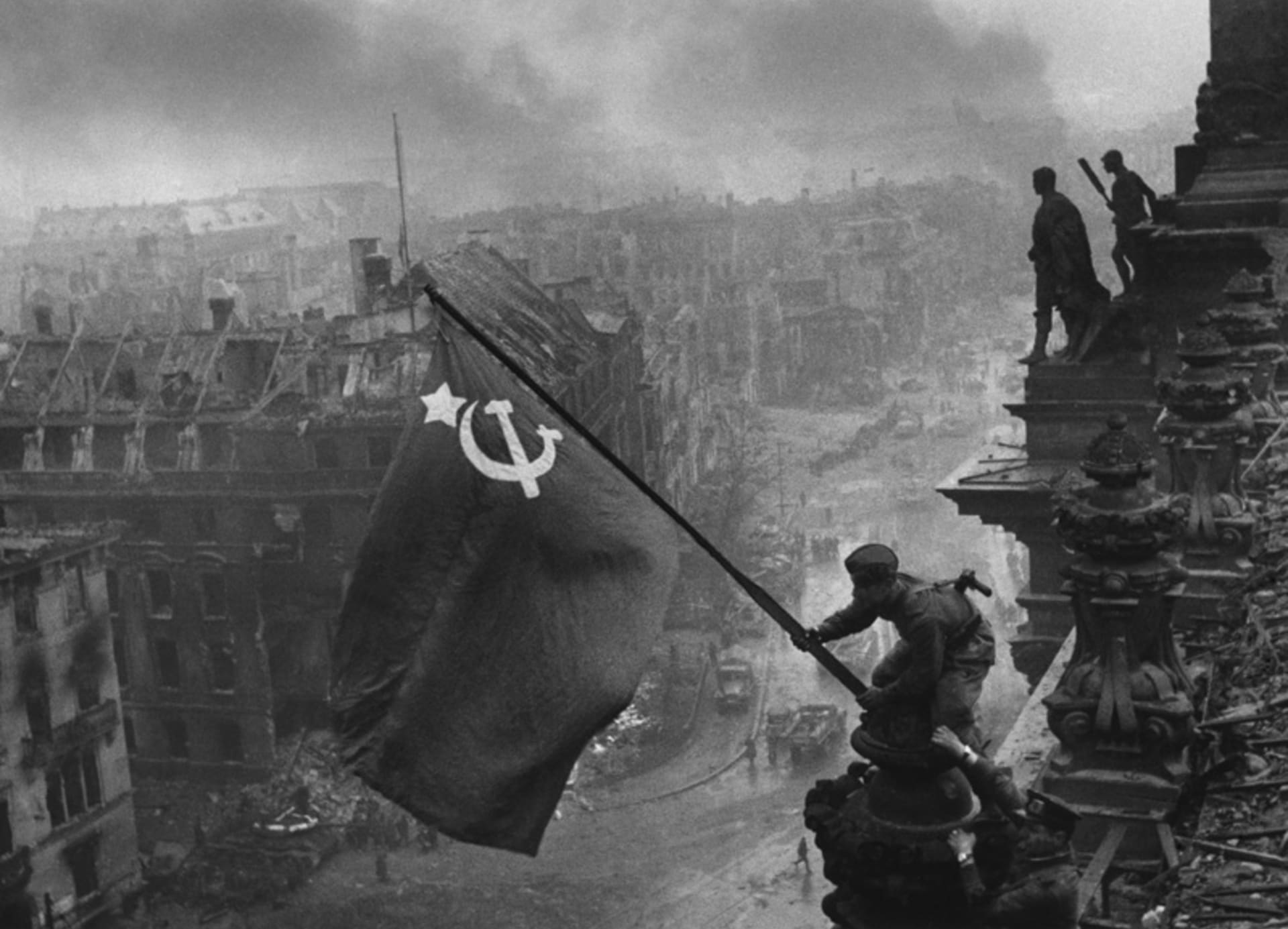 Sovětští vojáci vztyčují vlajku vítězství nad budovou Říšského sněmu v Berlíně. Válečný fotograf Jevgenij Anaňjevič Chalděj snímek aranžoval - vlajku původně vztyčil vojín Michail Minin 30. dubna 1945 ve 22:40, kdy už ovšem byla tma