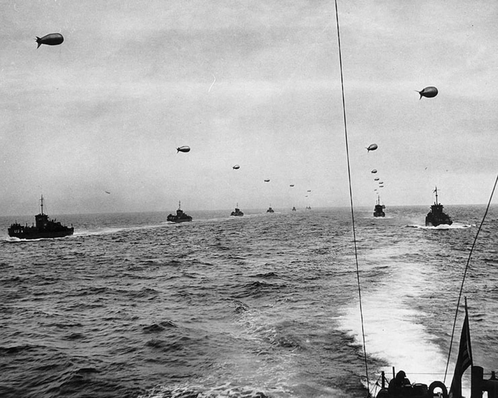 Velké vyloďovací lodě (LCI) se blíží 6. června 1944 k pobřeží Francie. Každá z lodí táhne balónovou baráž na ochranu před nepřátelským letectvem
