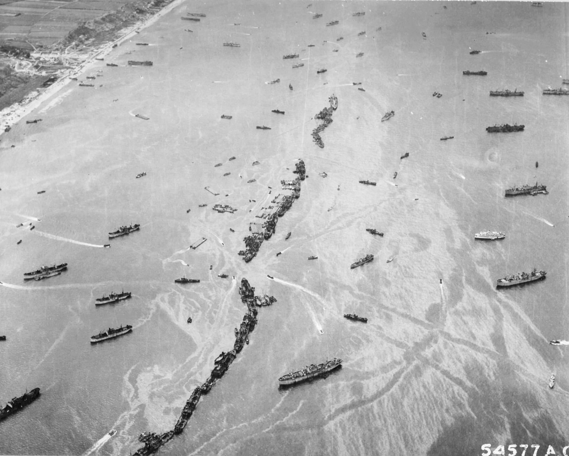 Americké lodě Liberty seřazené jedna za druhou tvoří provizorní vlnolam u pláže Omaha. je několik dnů po invazi a Spojencům zoufale chybí dobrý přístav