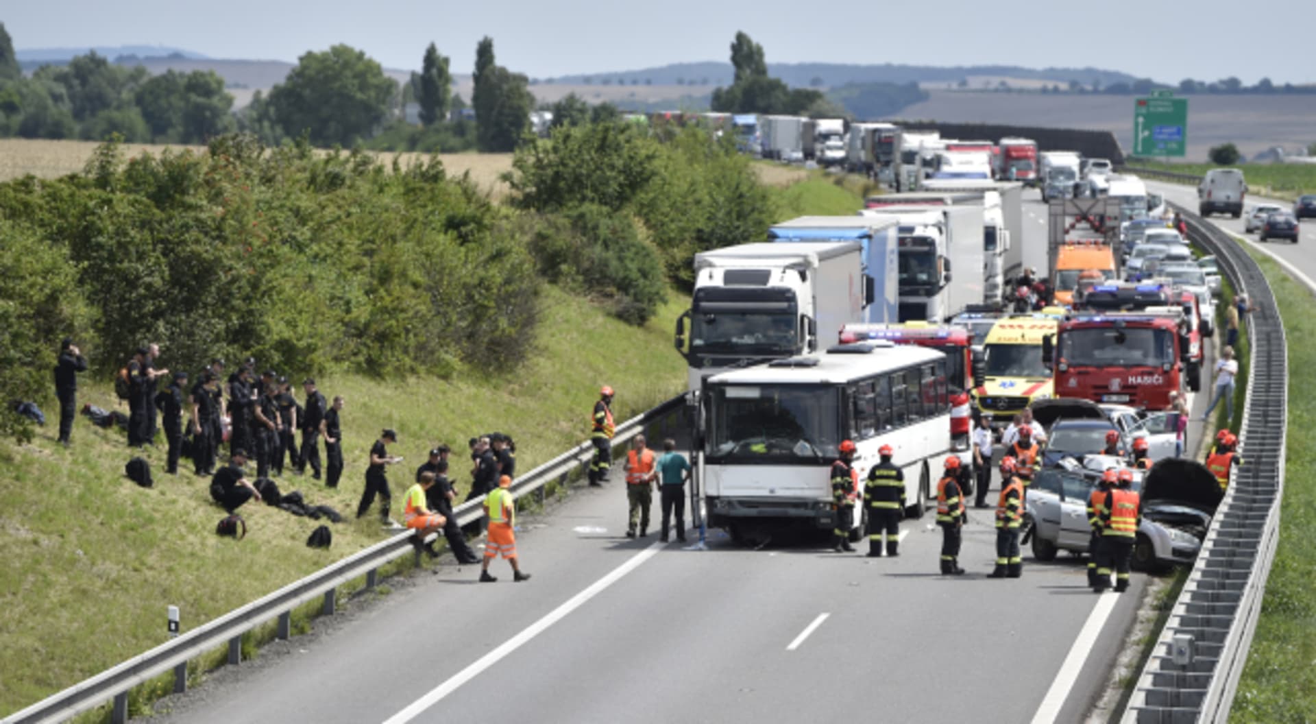 Policisté v černých uniformách postávají a posedávají ve stráni po nehodě jejich autobusu na dálnici D1 u Holubic na Vyškovsku. 