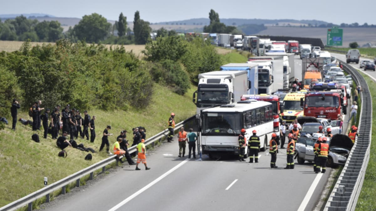 Policisté v černých uniformách postávají a posedávají ve stráni po nehodě jejich autobusu na dálnici D1 u Holubic na Vyškovsku. 