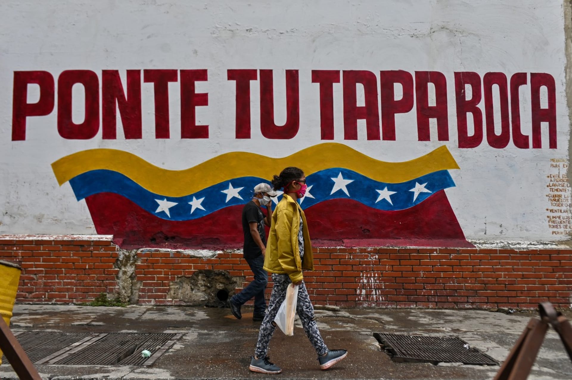 Lidé ve venezuelském hlavním městě Caracas chodí kolem nápisu vyzývajícího k nošení roušek.