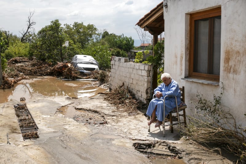 Starší žena sedí před zatopeným domem v obci Politika. 