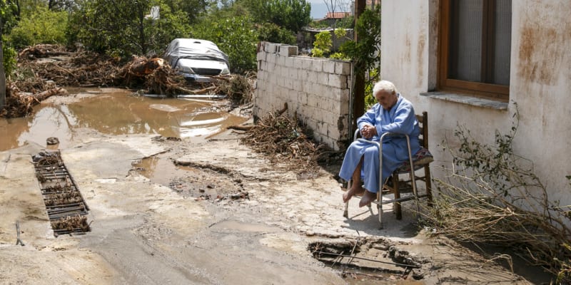 Starší žena sedí před zatopeným domem v obci Politika. 