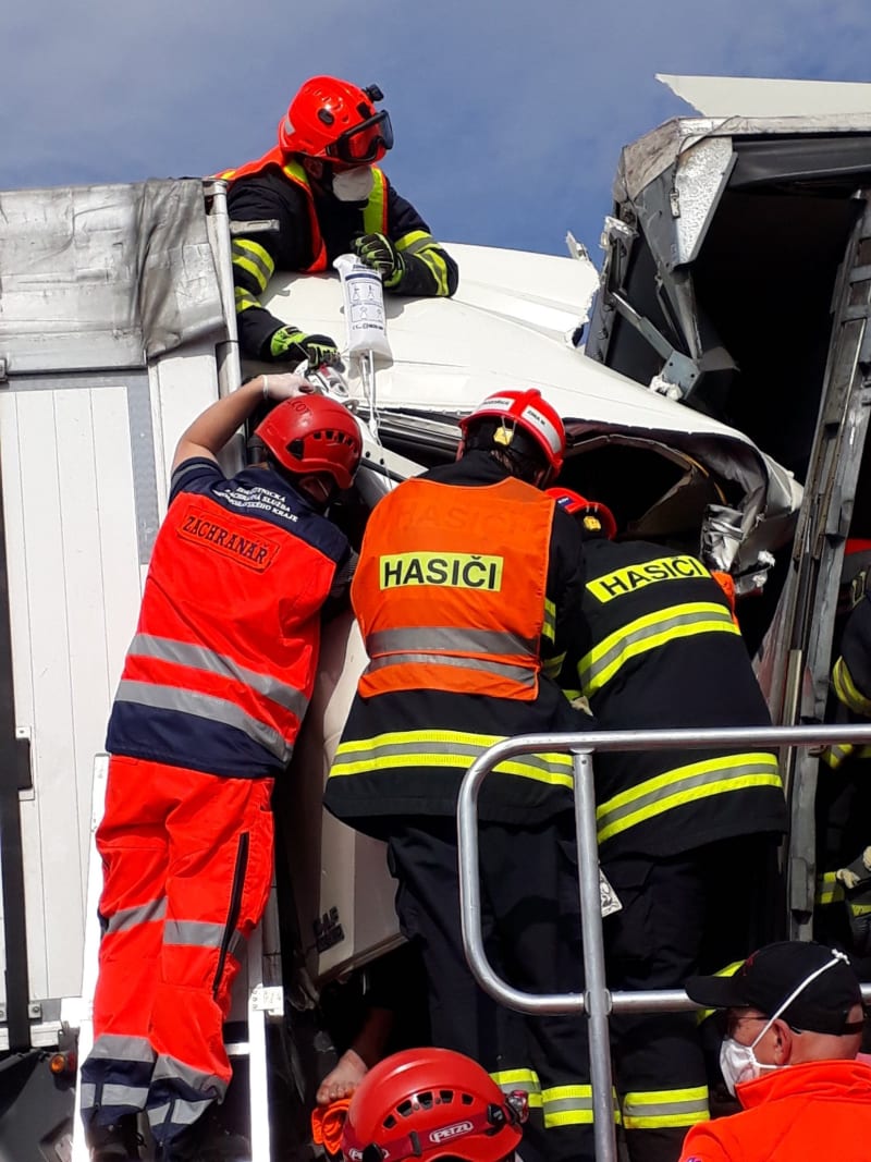 Hasiči a záchranáři se snaží poskytnout pomoc jednomu z řidičů kamionů, který po nehodě zůstal zaklíněný v kabině.