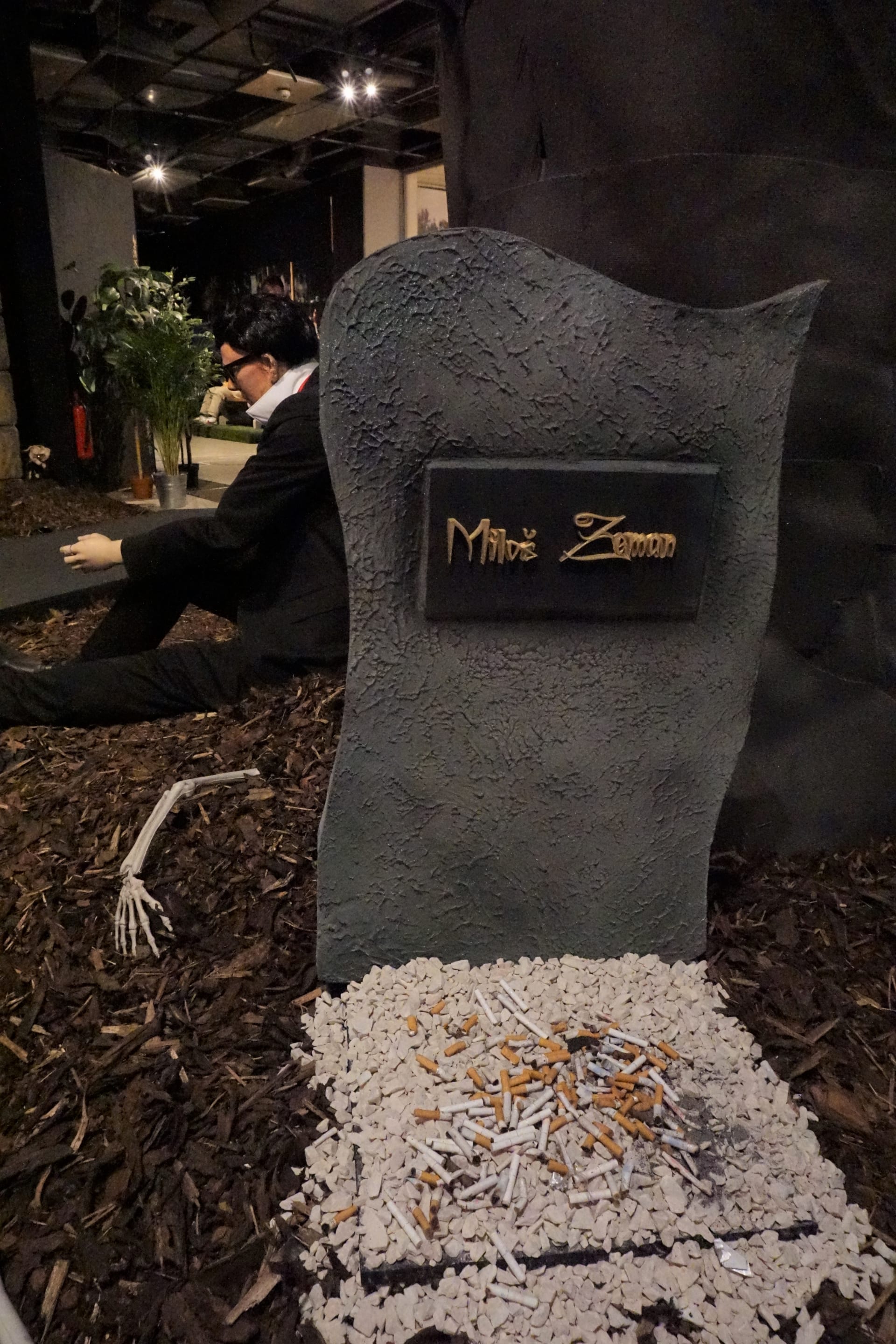 Hrob zde má i prezident Miloš Zeman, přestože je stále živ. Jeho místo posledního odpočinku pak doplňují vysypané cigarety, poněvadž je Zeman náruživým kuřákem. Kousek od jeho hrobu je pak vidět postava se zoufalým výrazem ve tváři, která se náramně podobná Zemanovu mluvčímu Jiřímu Ovčáčkovi.