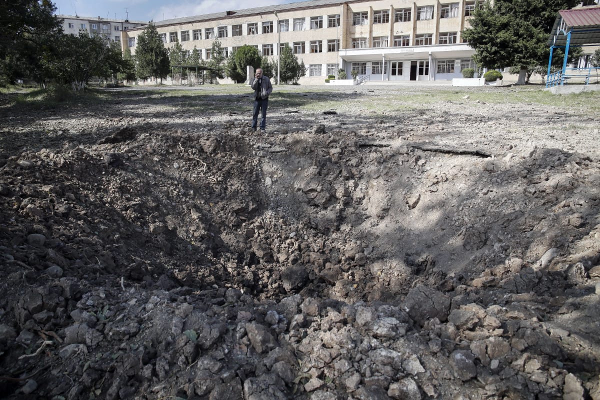 Muž stojí poblíž kráteru po explozi poblíž školy poté, co během vojenského konfliktu v Stepanakertu, separatistickém regionu Náhorního Karabachu, ostřelovalo území ázerbájdžánské dělostřelectvo. Fotografie ze soboty 10. října 2020. (foto: AP)