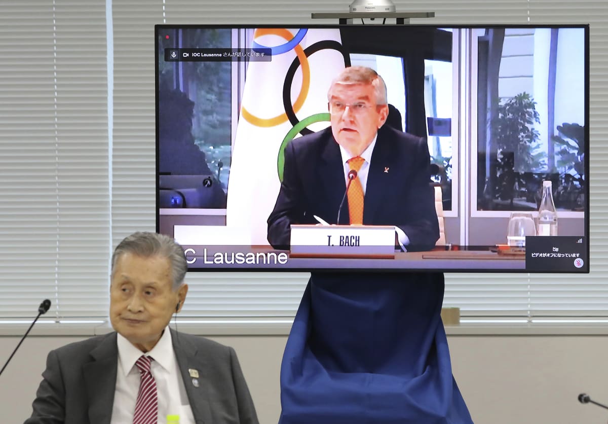 Prezident Mezinárodního olympijského výboru Thomas Bach (na obrazovce) mluví během videokonference s šéfem organizačního výboru olympijských her 2021 v Tokiu Joširem Morim. (vlevo dole)
