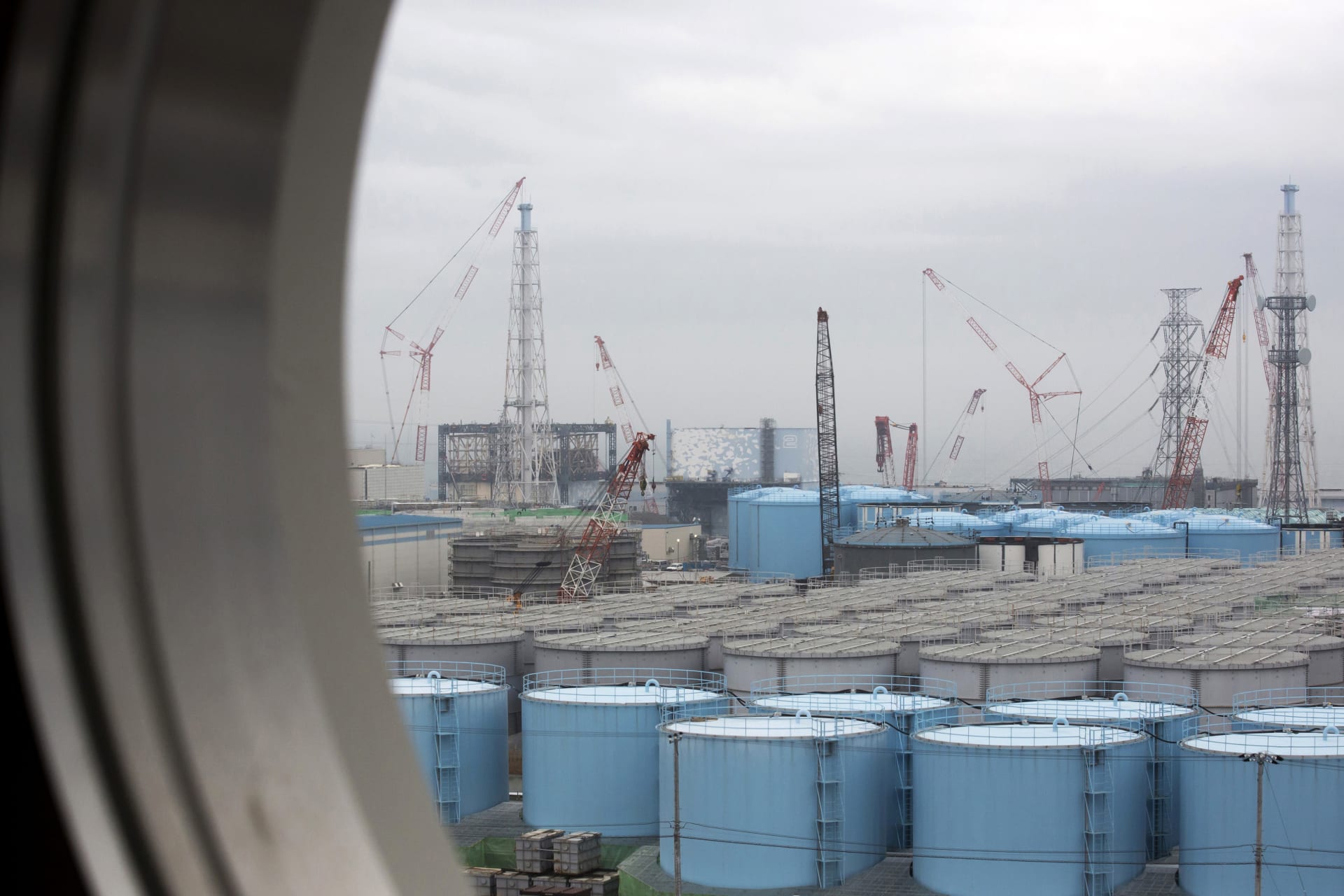 Skladovací nádrže na kontaminovanou vodu v průhledu skrz okno budovy jaderné elektrárny Fukušima v prefektuře Fukušima na severovýchodě Japonska (Zdroj: AP)