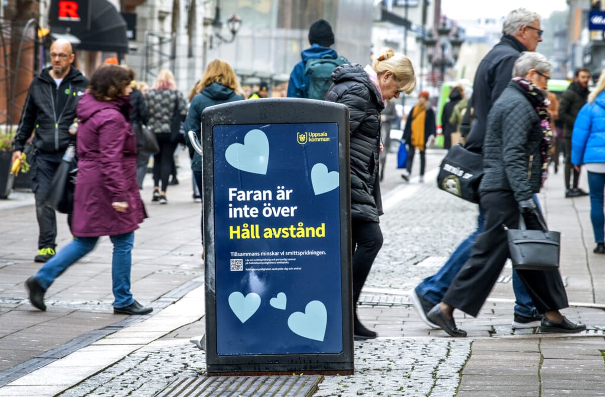 Lidé ve švédské Uppsale chodí kolem cedule s nápisem „Nebezpečí ještě neskončilo – udržujte odstup“. 