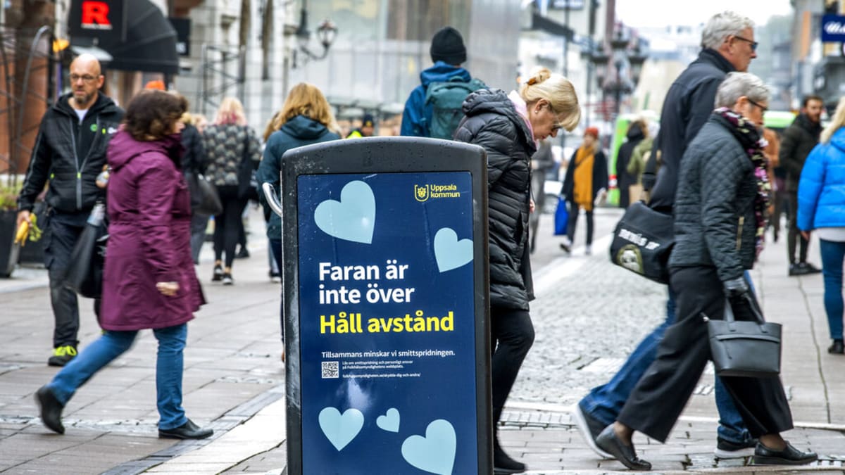Lidé ve švédské Uppsale chodí kolem cedule s nápisem „Nebezpečí ještě neskončilo – udržujte odstup“. 