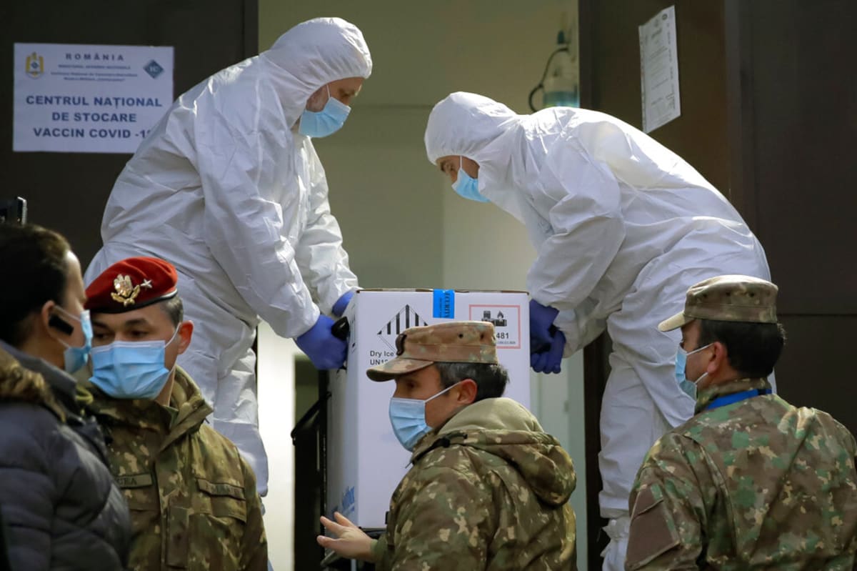 Ilustrační fotografie: Rumunští pracovníci v ochranných oblecích přenášejí krabici s vakcínami proti COVID-19.