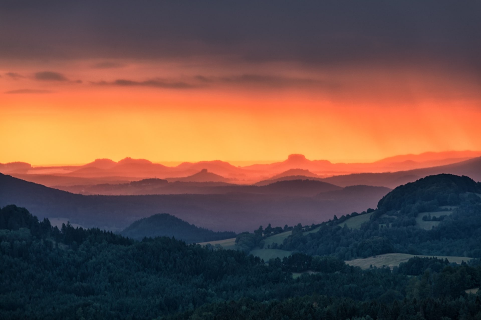 Fotografický obraz kopcovité krajiny fascinuje barevnou hrou při západu slunce