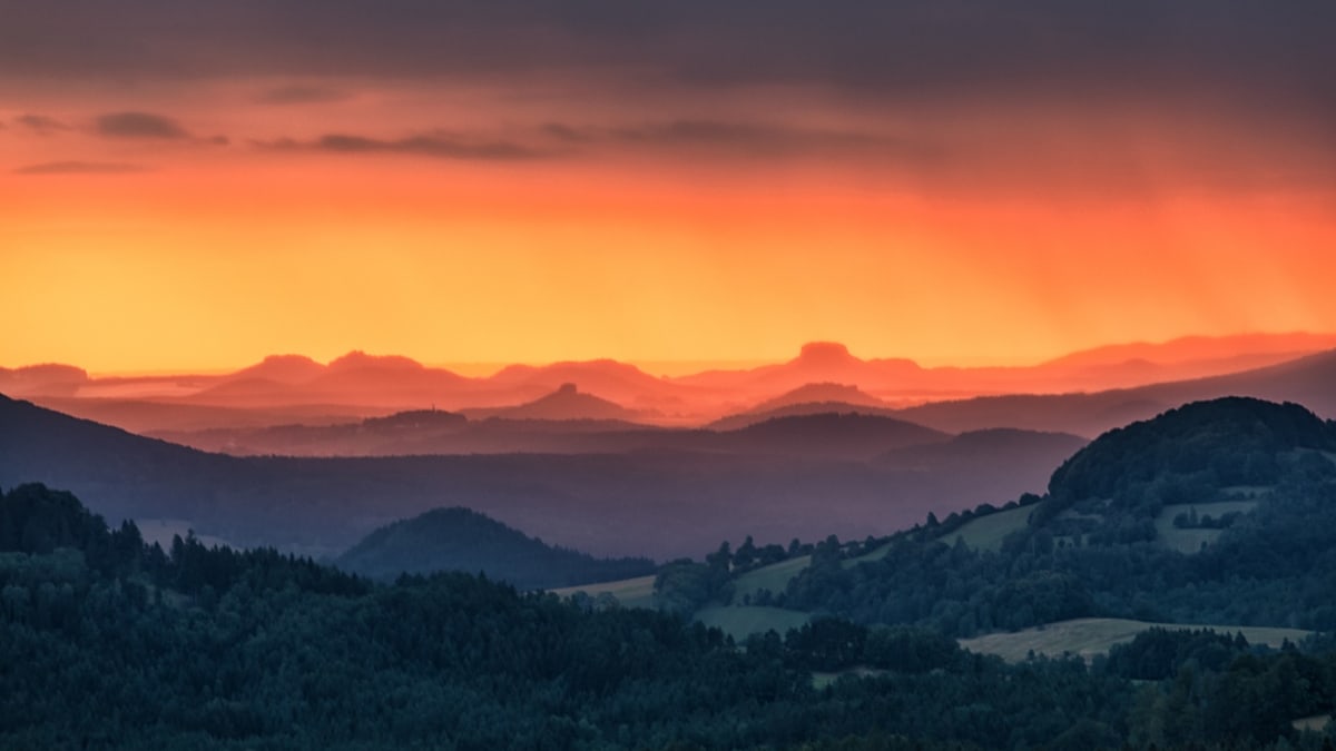 Fotografický obraz kopcovité krajiny fascinuje barevnou hrou při západu slunce