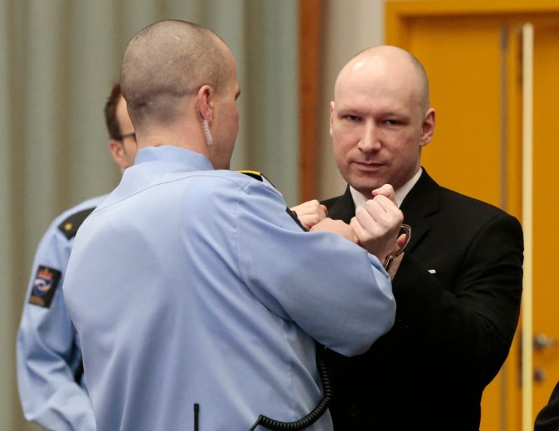 Policista sundavá pouta Andersi Breivikovi u soudu.