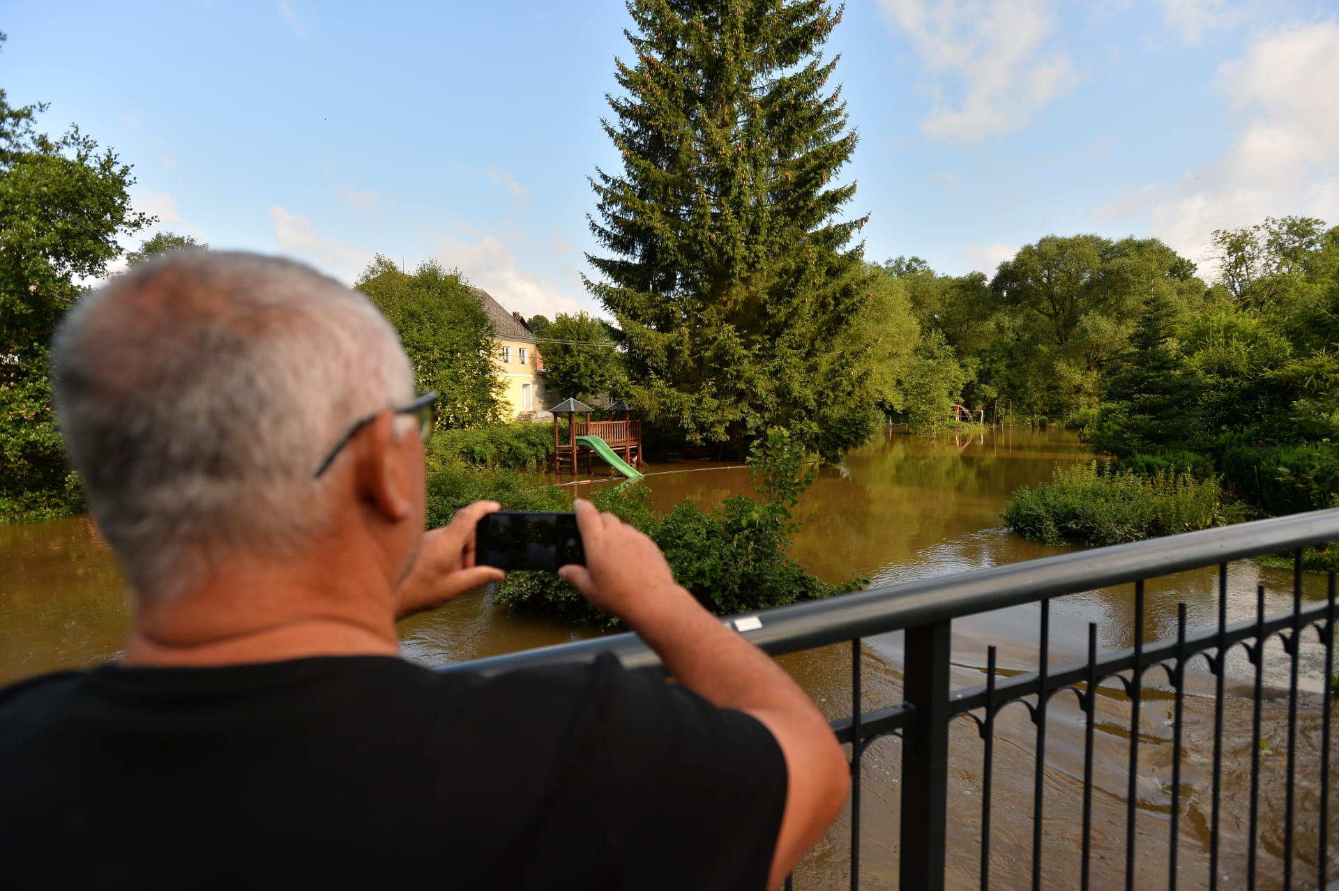 Muž v Dobranově v České Lípě fotografuje Dobranovský potok, který se po silných deštích vylil z břehů.