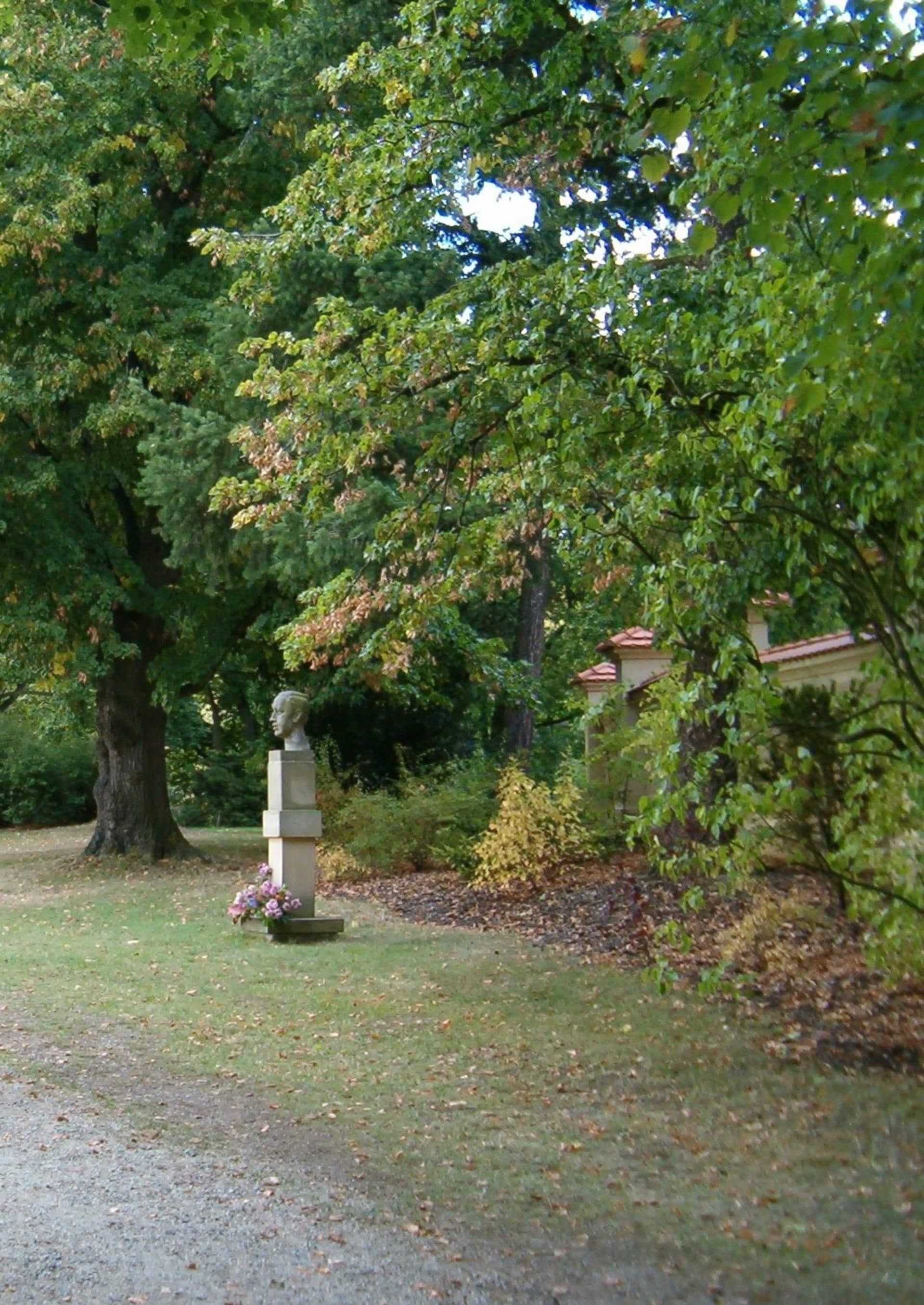 Busta Karla Čapka stojí na pravé straně cesty, pár kroků od vstupní brány