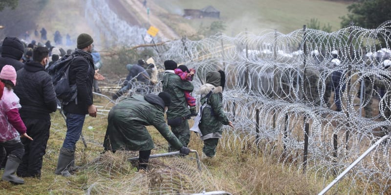 Stovky migrantů se snaží poškodit plot s ostnatým drátem na bělorusko-polské hranici.