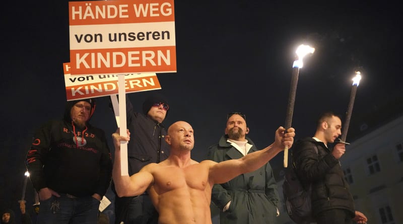 Polonahý muž protestuje ve Vídni proti povinnému očkování proti koronaviru s transparentem „ruce pryč od našich dětí“.