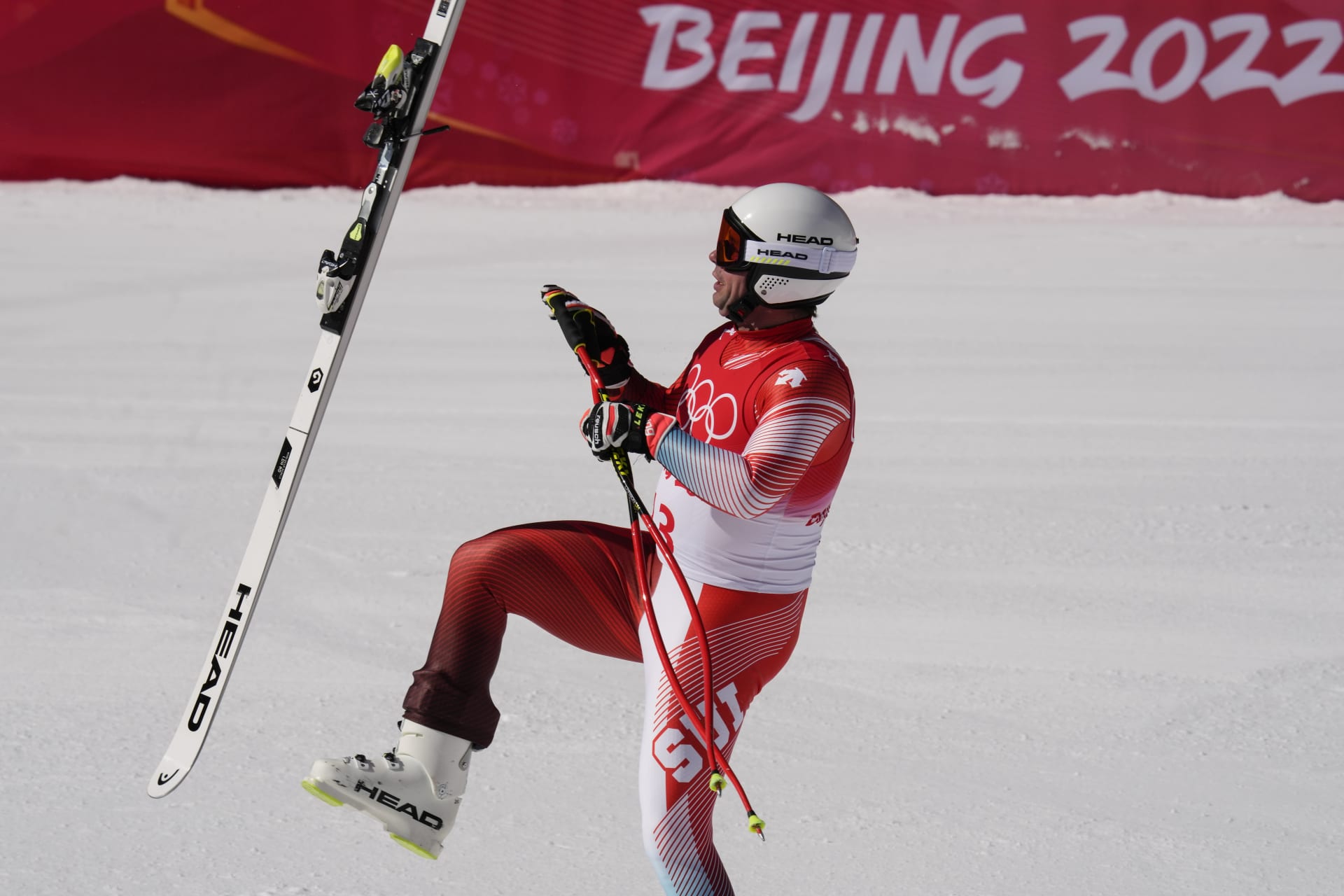 Švýcarský sjezdař Beat Feuz chytá vykopnutou lyži v cíli olympijského závodu 2022 a vzdává tím holt svému krajanovi Didieru Cuchemu, mistru světa v super-G a stříbrnému na olympiádě 1998 v Naganu. 