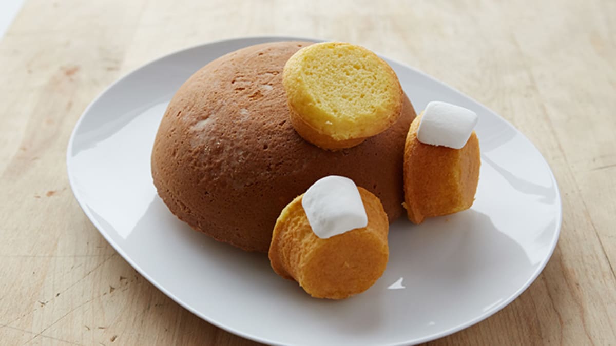 Muffinům lehce seřízněte vršky. Půlkulatý korpus položte na talíř vypouklou stranou nahoru a přilepte na něj pomocí krému muffiny. Na dva muffiny po stranách pak ještě přilepte murshmallow.