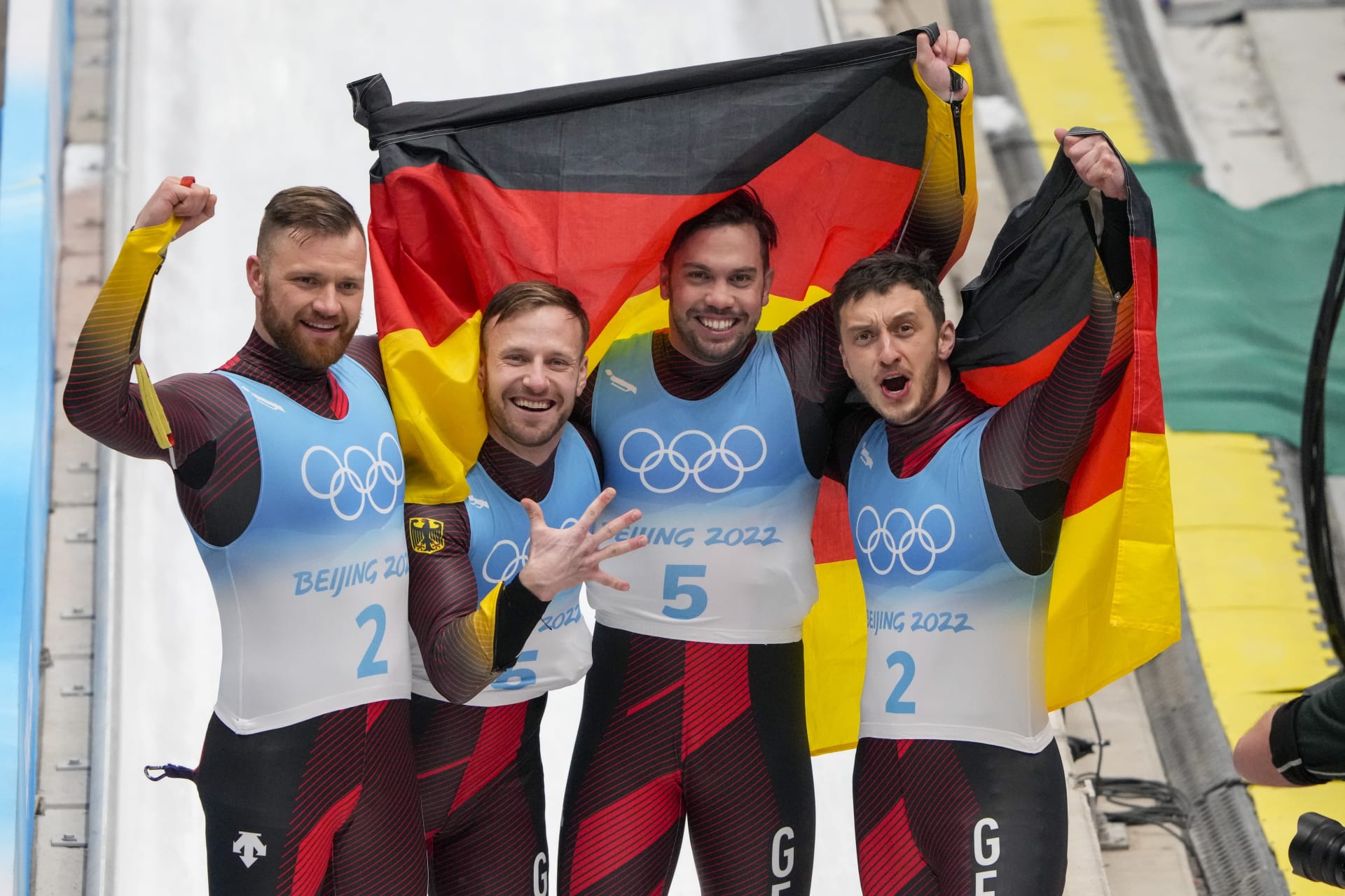 Takto se čtyři němečtí sáňkaři Tobias Arlt a Tobias Wendl, Sascha Benecken a Toni Eggert(zleva) radovali v cíli ze zlatých a stříbrných medailí na zimních olympijských hrách 2022 než mezi ně vstoupil prezident Mezinárodního olympijského výboru Thomas Bach.