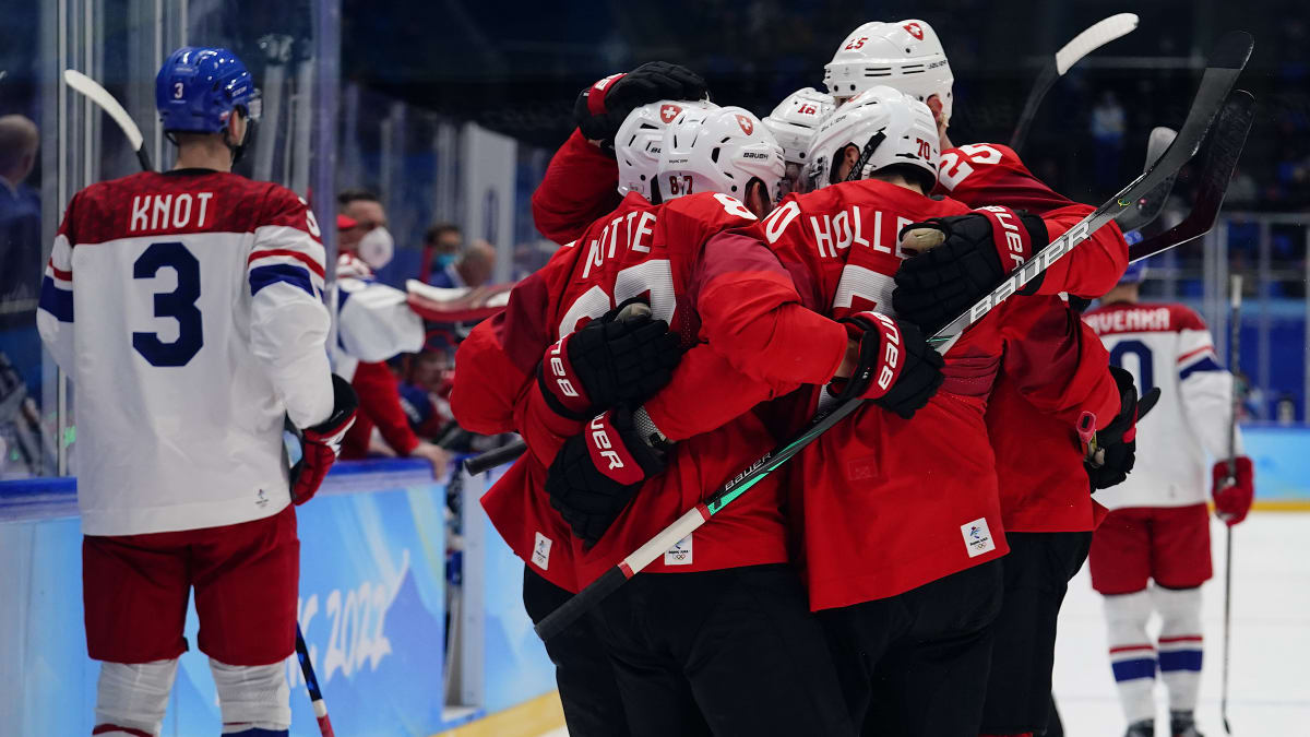 Švýcarští hokejisté se radují z branky a postupu do čtvrtfinále olympijského turnaje 2022. Vlevo přihlíží český obránce Ronald Knot.