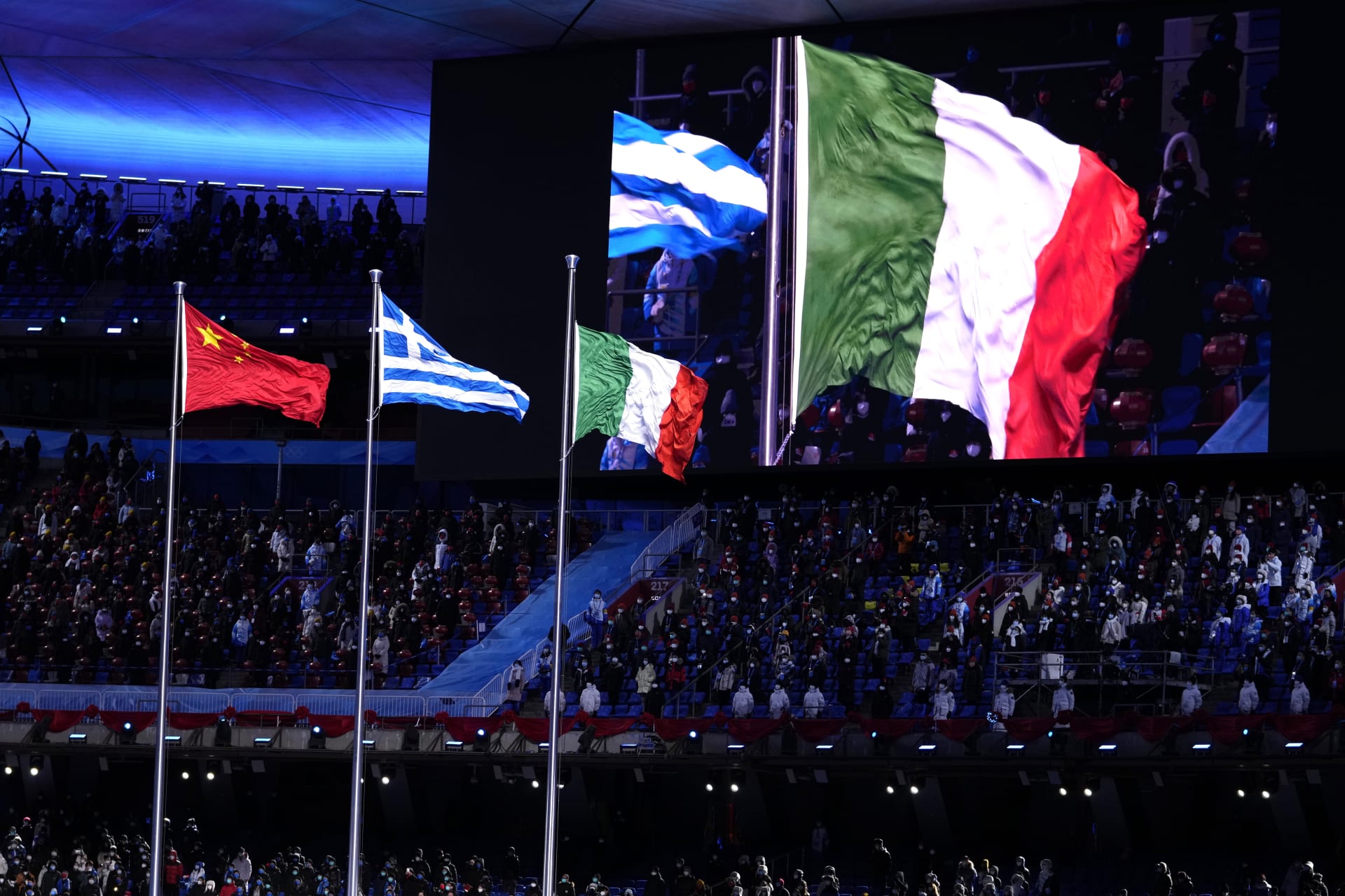 Slavnostní ceremoniál k ukončení ZOH 2022. Čínská vlajka pro pořadatele končících her, řecká coby kolébka olympijských her a italská pro budoucí pořadatele. Další turnaj pod pěti kruhy se zimními sporty se totiž v roce 2026 koná v italském Miláně a Cortině d'Ampezzo.