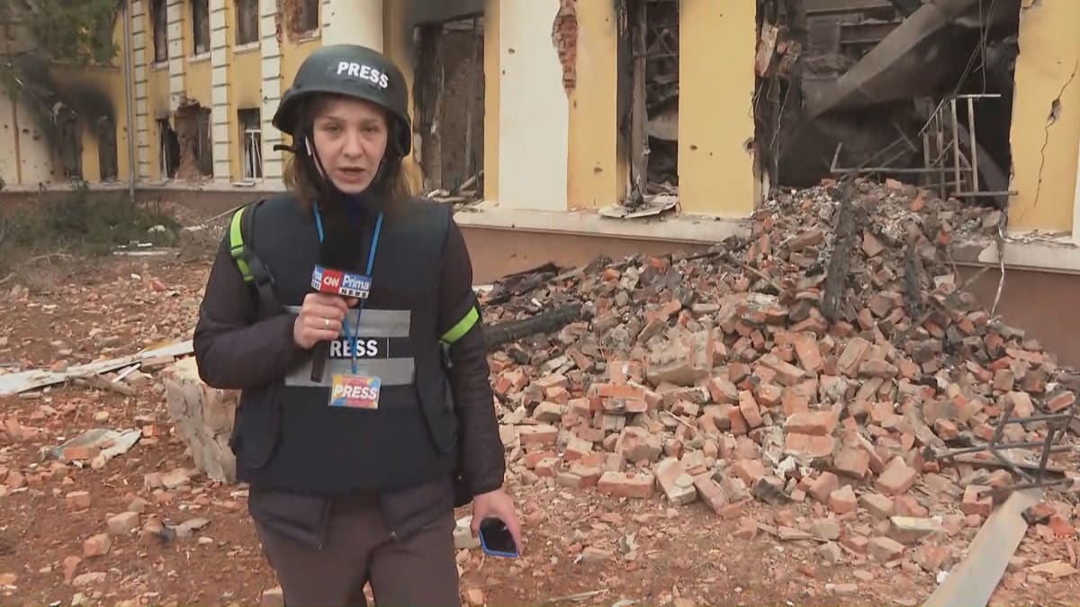 Reportérka CNN Prima NEWS Darja Stomatová stojí vedle zničené charkovské školy.