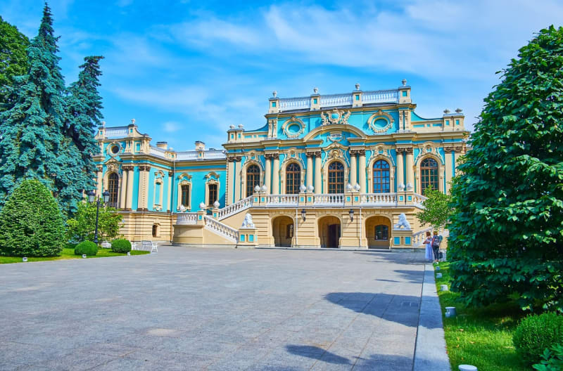 Malebná zelená zahrada Mariinského paláce s výhledem na barokní fasádu, bohatě zdobená štukem, Kyjev, Ukrajina
