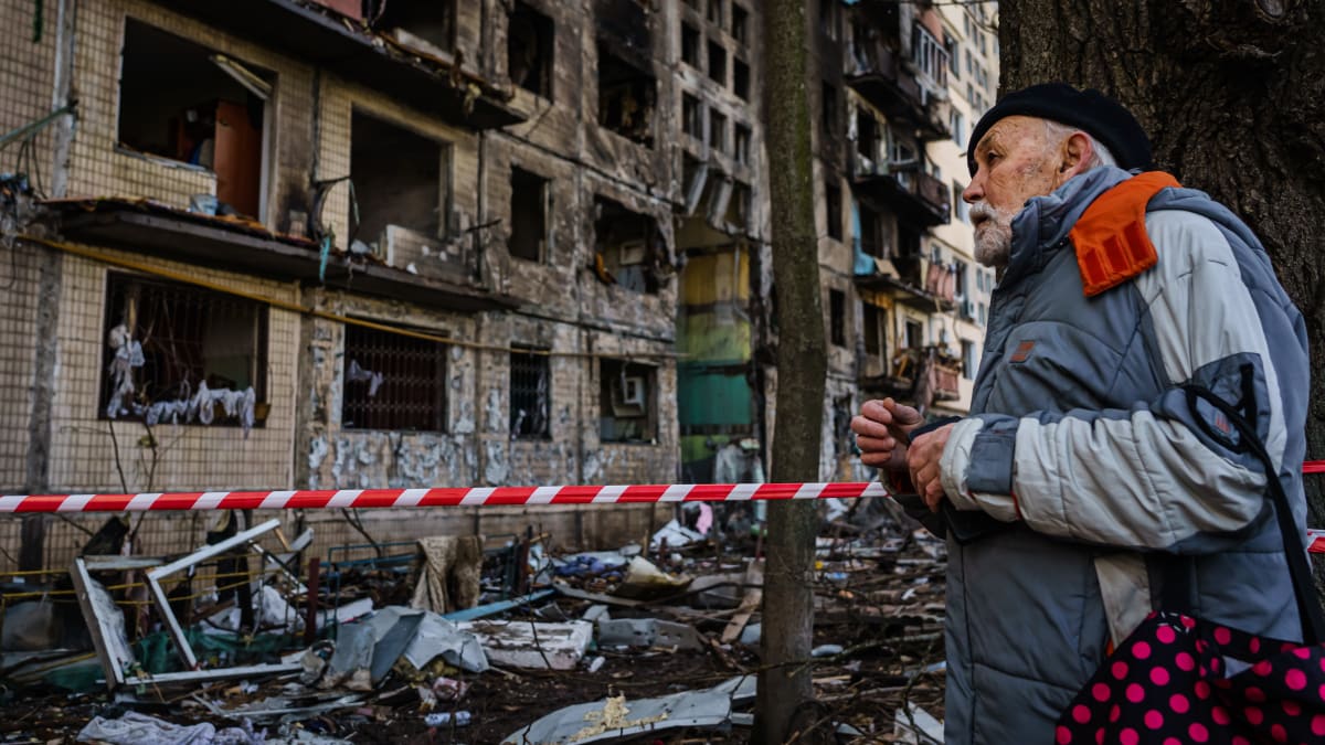 Muž se dívá na poškozený bytový dům, který byl podle kyjevských úřadů poškozen ruským bombardováním.