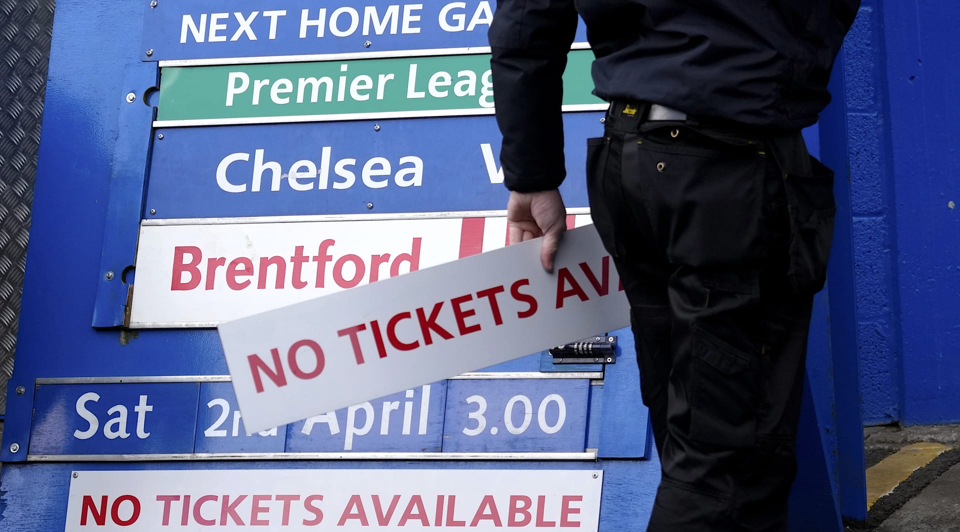 Zřízenec fotbalového klubu Chelsea Londýn odnáší cedulku „Vstupenky nejsou“ z tabule u vchodu stadionu Stamford Bridge poté, co britská vláda zmírnila sankce vůči majiteli Romanu Abramovičovi.