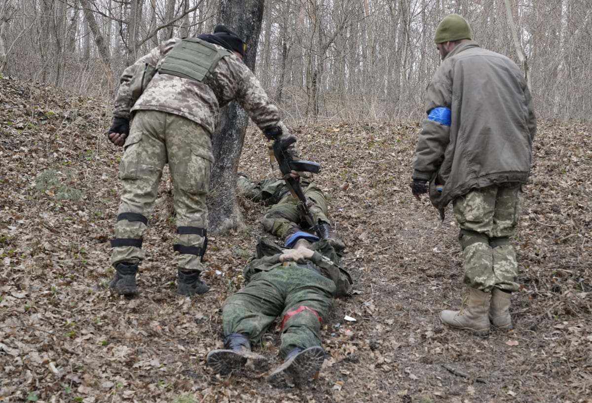 Ukrajinští vojáci prohledávají tělo mrtvého ruského vojáka po střetu ve městě Trosťanec v Sumské oblasti.  (28. března 2022)
