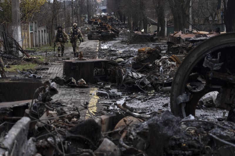 Vojáci se procházejí mezi zničenými ruskými tanky v Buči.