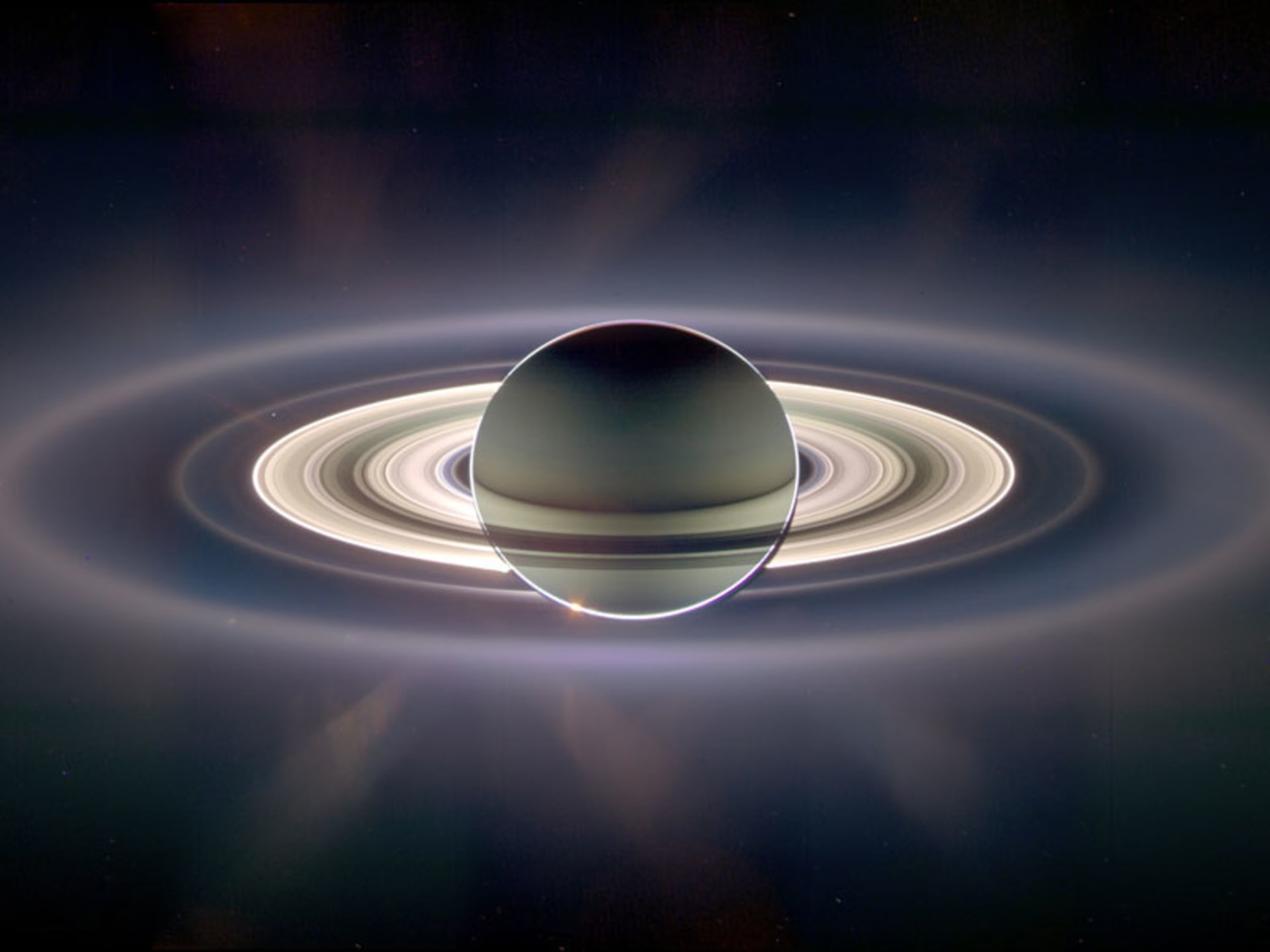 : Saturn jak jej vidí vesmírná sonda Cassini proti Slunci. Peggy se vytvořila na vnějším okraji jasných prstenců. Na snímku je nicméně vidět mnoho dalších méně jasných prstenců, které dávají tušit dávné existenci mnohem většího prstencového komplexu