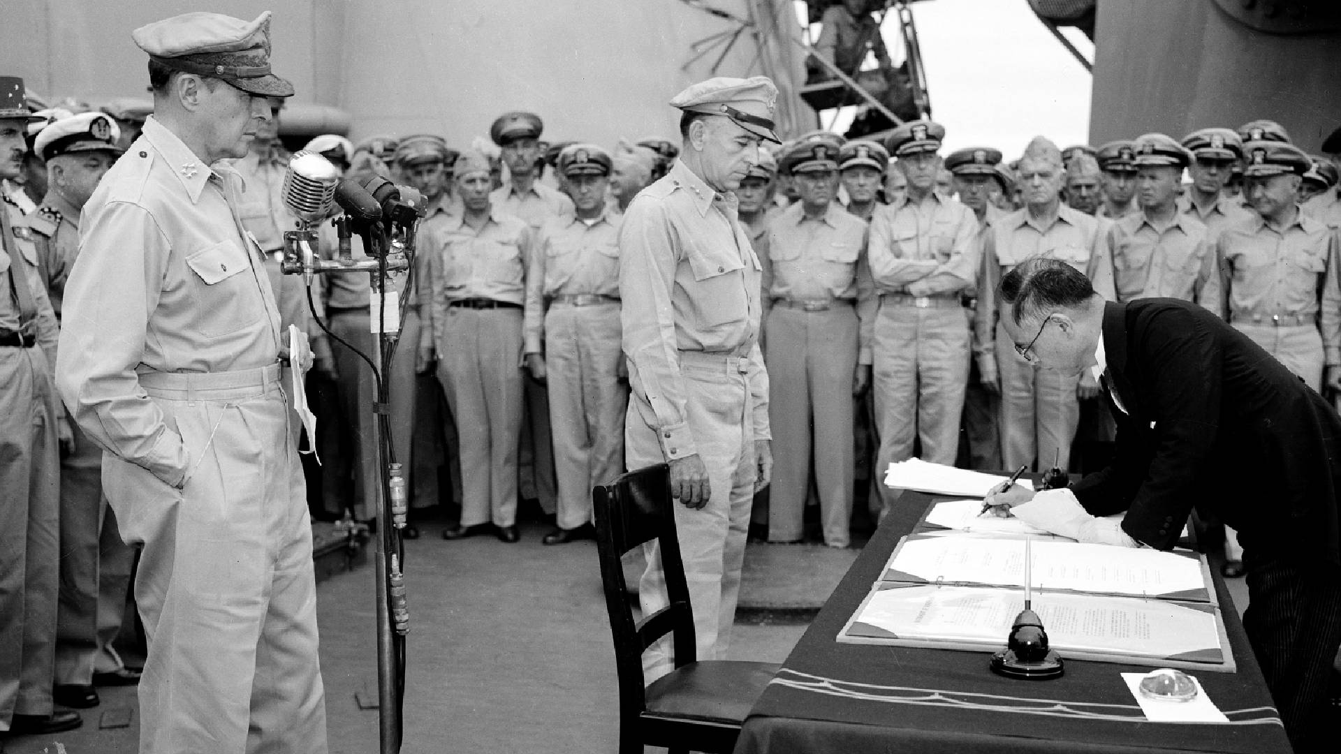 Generál Douglas MacArthur (vlevo) přihlíží podpisu kapitulace Japonska