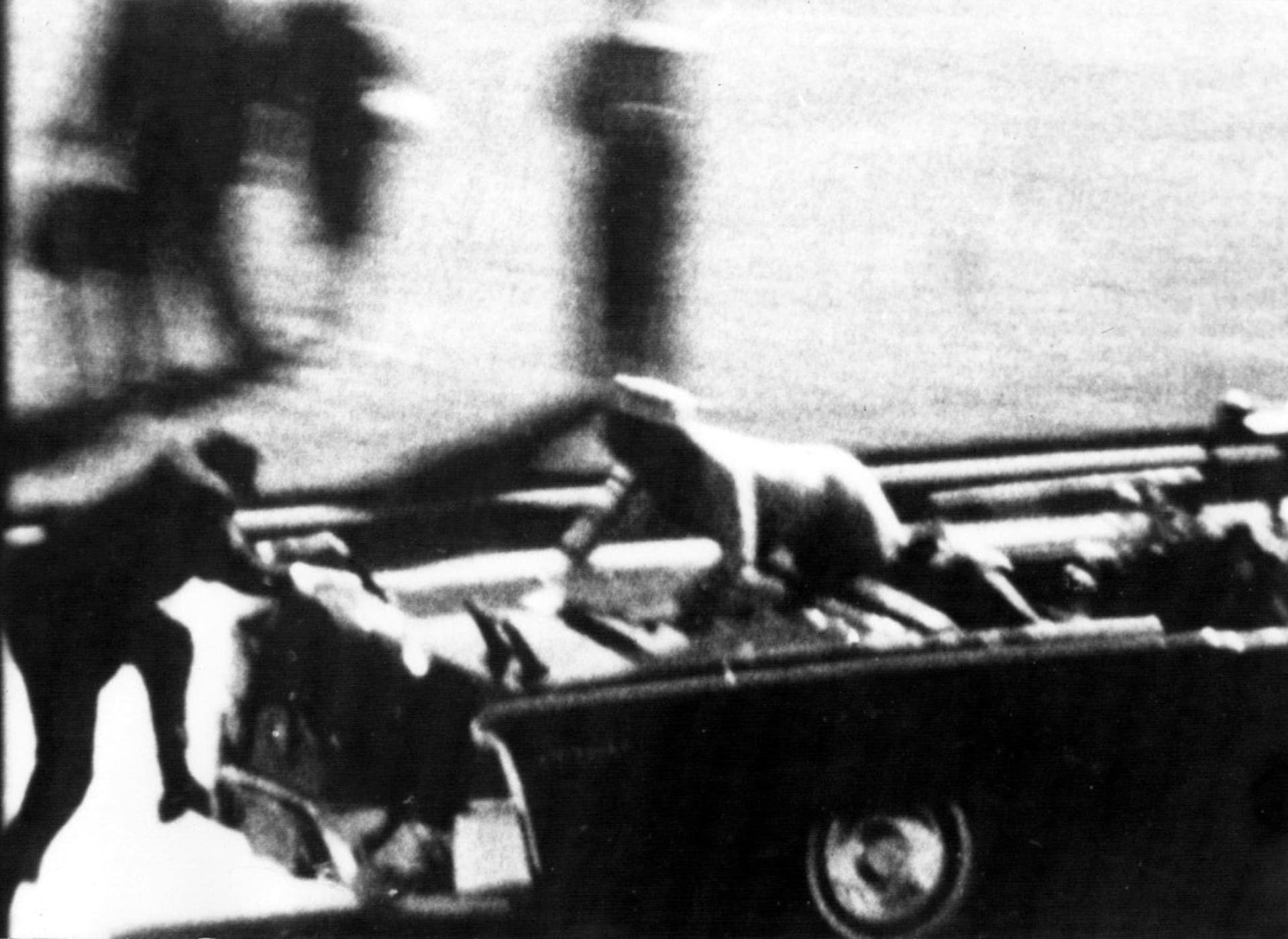 Krátce po atentátu - Jackie Kennedyová volá o pomoc pro smrtelně zraněného manžela, zezadu se snaží naskočit člen ochranky.