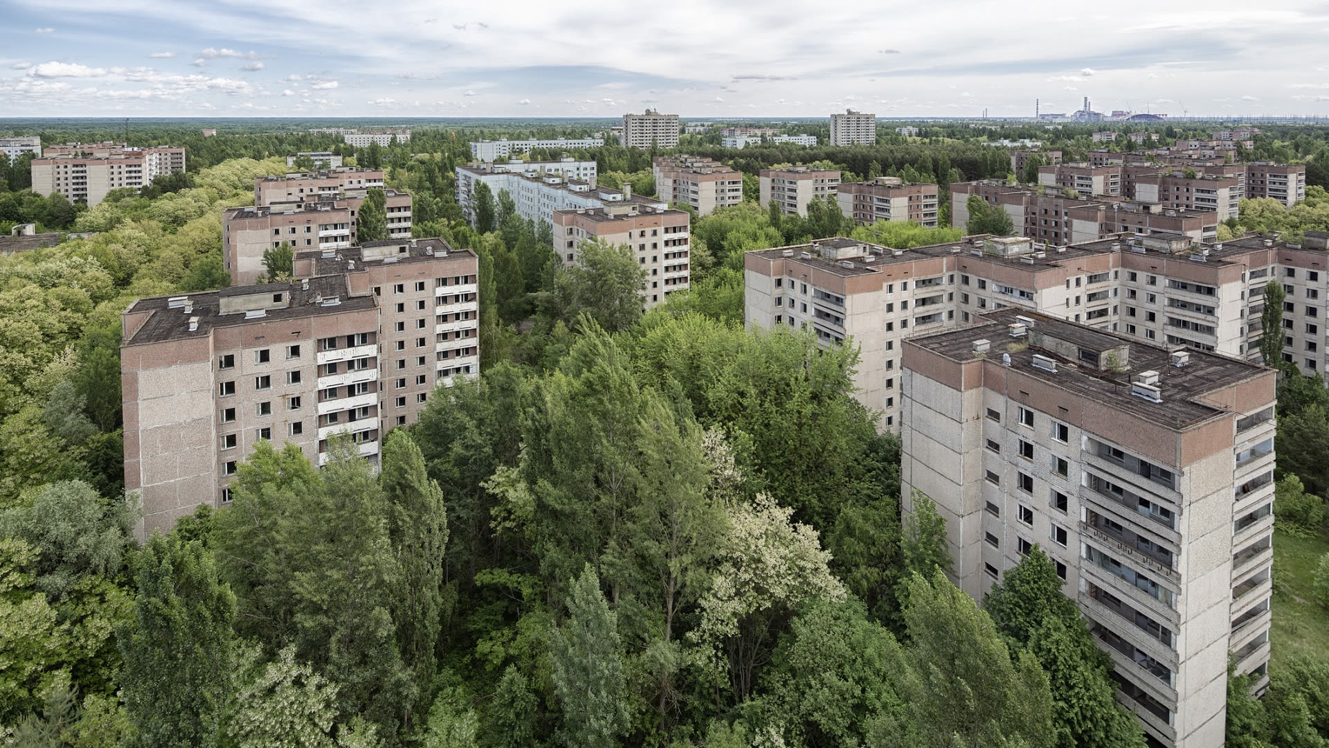 Město Pripjať se siluetou černobylské elektrárny na obzoru postupně pohlcuje zeleň