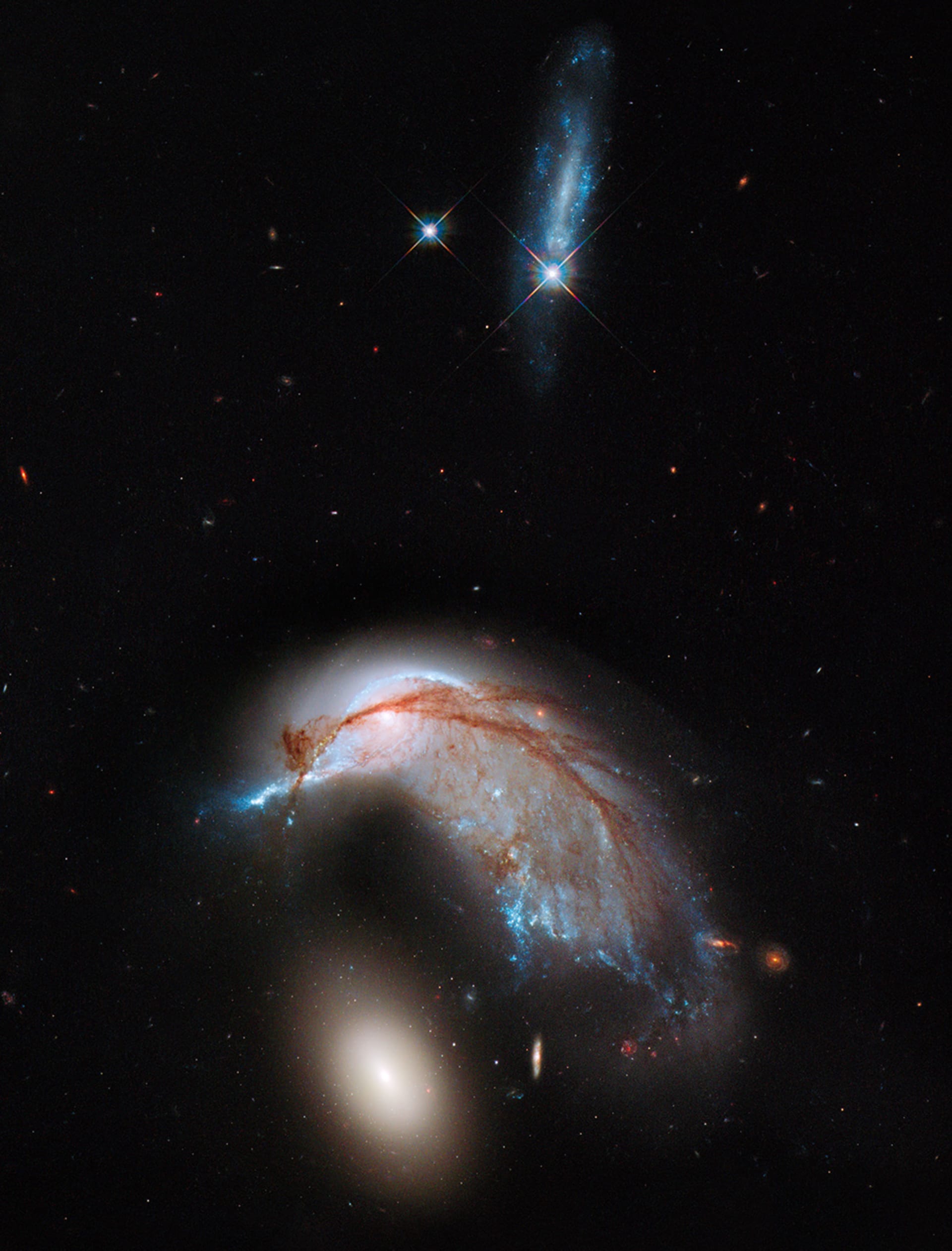 Snímek z Hubbleova teleskopu zachytil kolizi dvou galaxií. Gravitační síla eliptické galaxie NGC 2937 (vlevo dole) „vytahuje“ v divokých proudech prach a plyn ze spirálové galaxie NGC 2936
