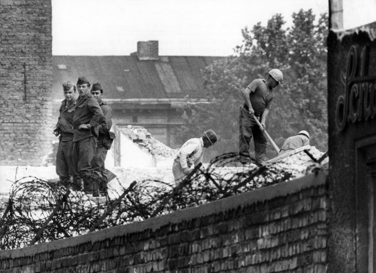 Stavební dělníci pod bedlivým dohledem příslušníků východoněmecké armády likvidují hraniční dům na Bernauer Straße (1. června 1966)