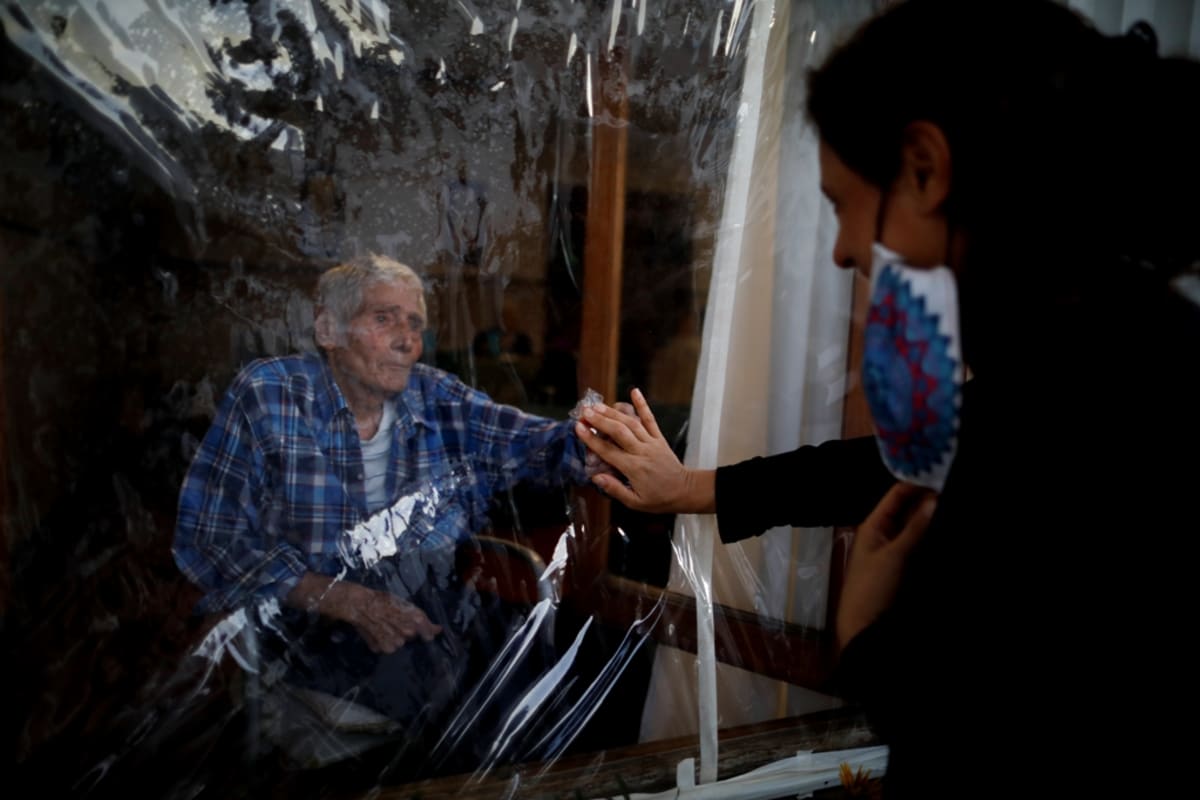 Victor Tripiana (86) se v domově pro seniory v argentinském Tandilu dotýká 4. dubna 2021 přes průhledný závěs dlaně své snachy. Opatření proti šíření nemoci covid-19 po celém světě těžce dopadla hlavně na seniory