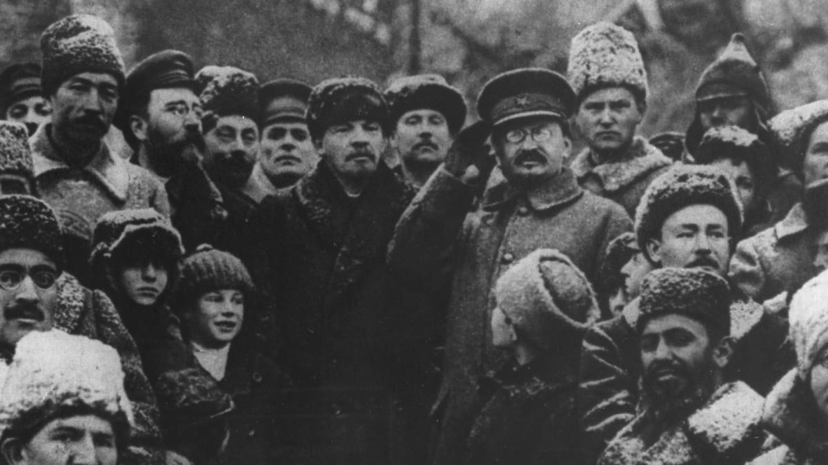 Lev Kameněv (vzadu vlevo s vousem a brýlemi), V. I. Lenin (uprostřed) a salutující Lev Trockij v říjnu 1917