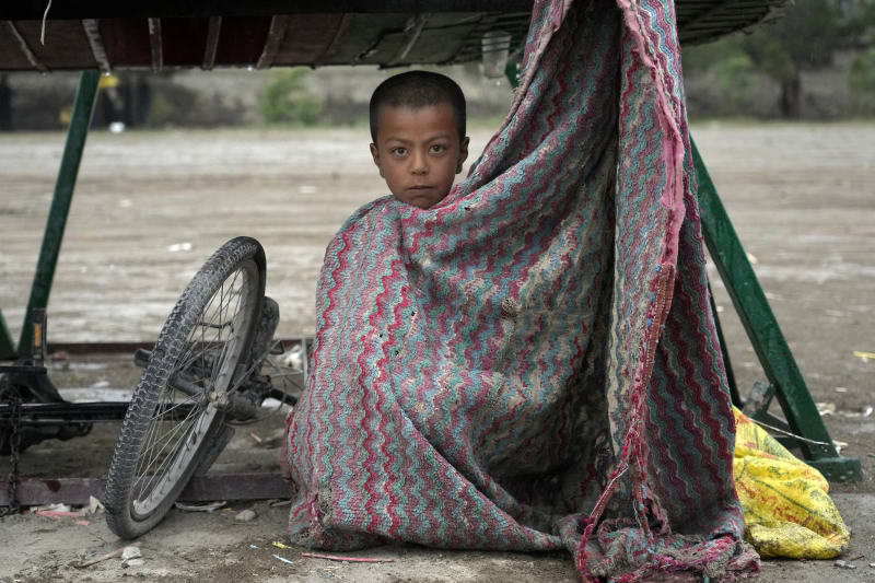 Dítě se schovává před deštěm pod trakařem v afghánském Kábulu, úterý 3. května 2022. 