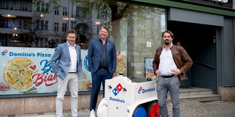 Daniel Richart, Andre ten Wolde a Geert-Jan van Nunen (zprava) ze společnosti Teraki pózují s robotem na doručování pizzy před pobočkou pizzerie Dominos Pizza Deutschland.
