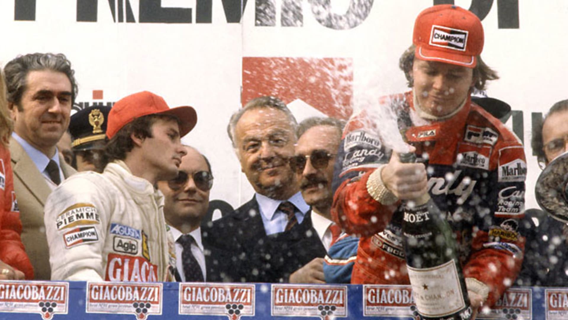 Zrazený Villeneuve na stupních vítězů Imole 14 dnů před osudnou nehodou. Vpravo oslavuje vítěz Pironi, který si však dlouhého života také neužil.