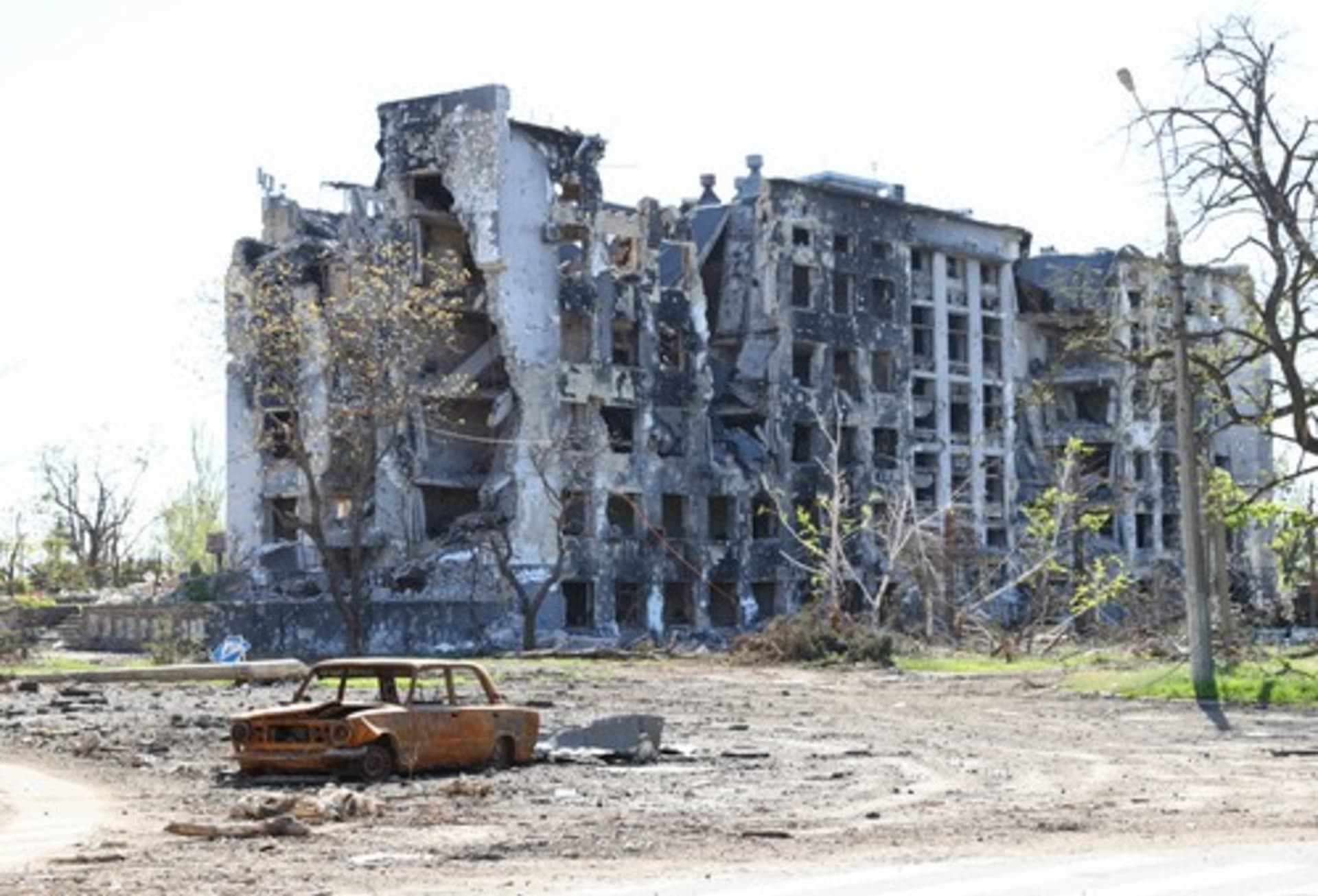 Ohořelý vrak auta před zničenými obytnými budovami v Mariupolu
