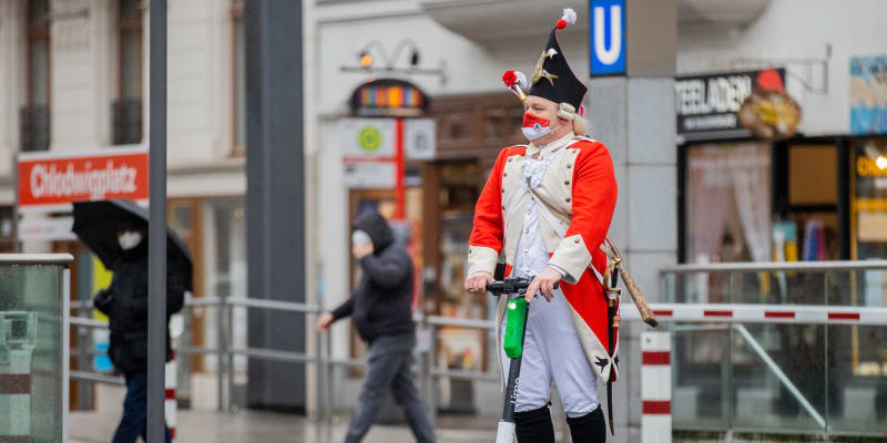Muž v převleku přijíždí k zahájení tradičního karnevalu v německém Kolíně nad Rýnem na elektrické koloběžce.