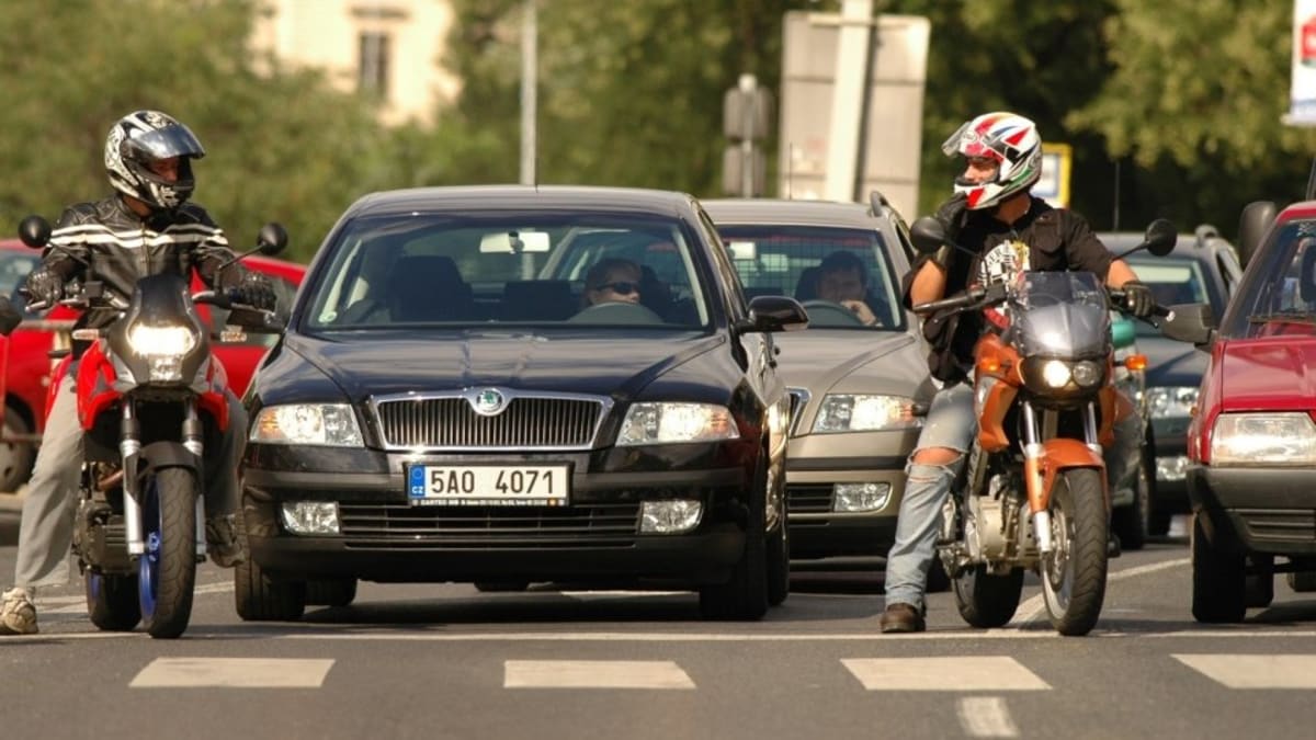 Běžný obrázek městských ulic v teplé části roku: Motocykly nacpané v těsných mezerách mezi auty připraveni vyrazit na zelenou jako první.