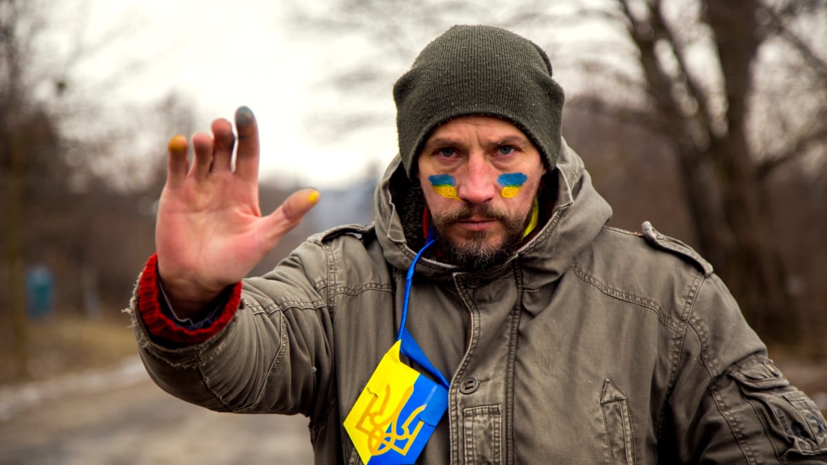 Ukrajinský bojovník kontrolující vozy na poničené silnici (7. 3. 2022)